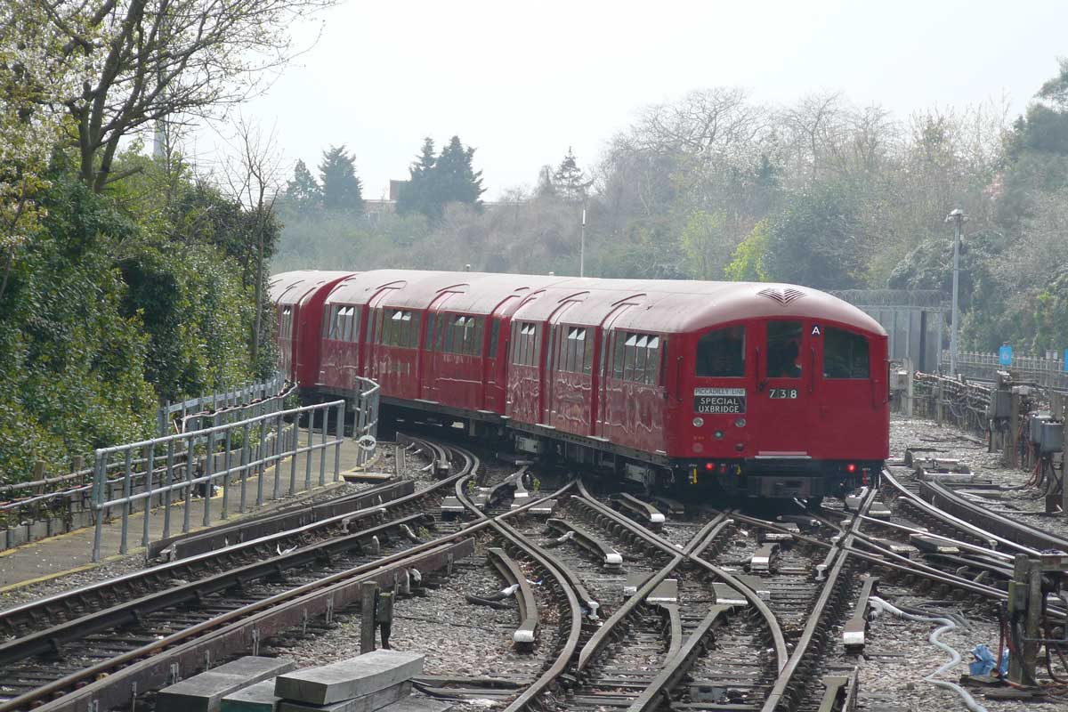 A 1938 stock Underground train in red livery on the Piccadilly line, its destination blind reading Piccadilly Line Special Uxbridge, coming off a set of points