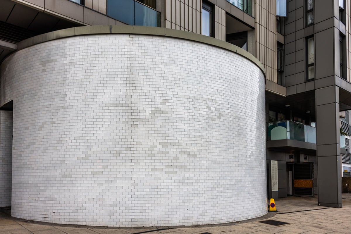 A white-tiled circular shelter entrance rotunda on a south London street beside a modern apartment block