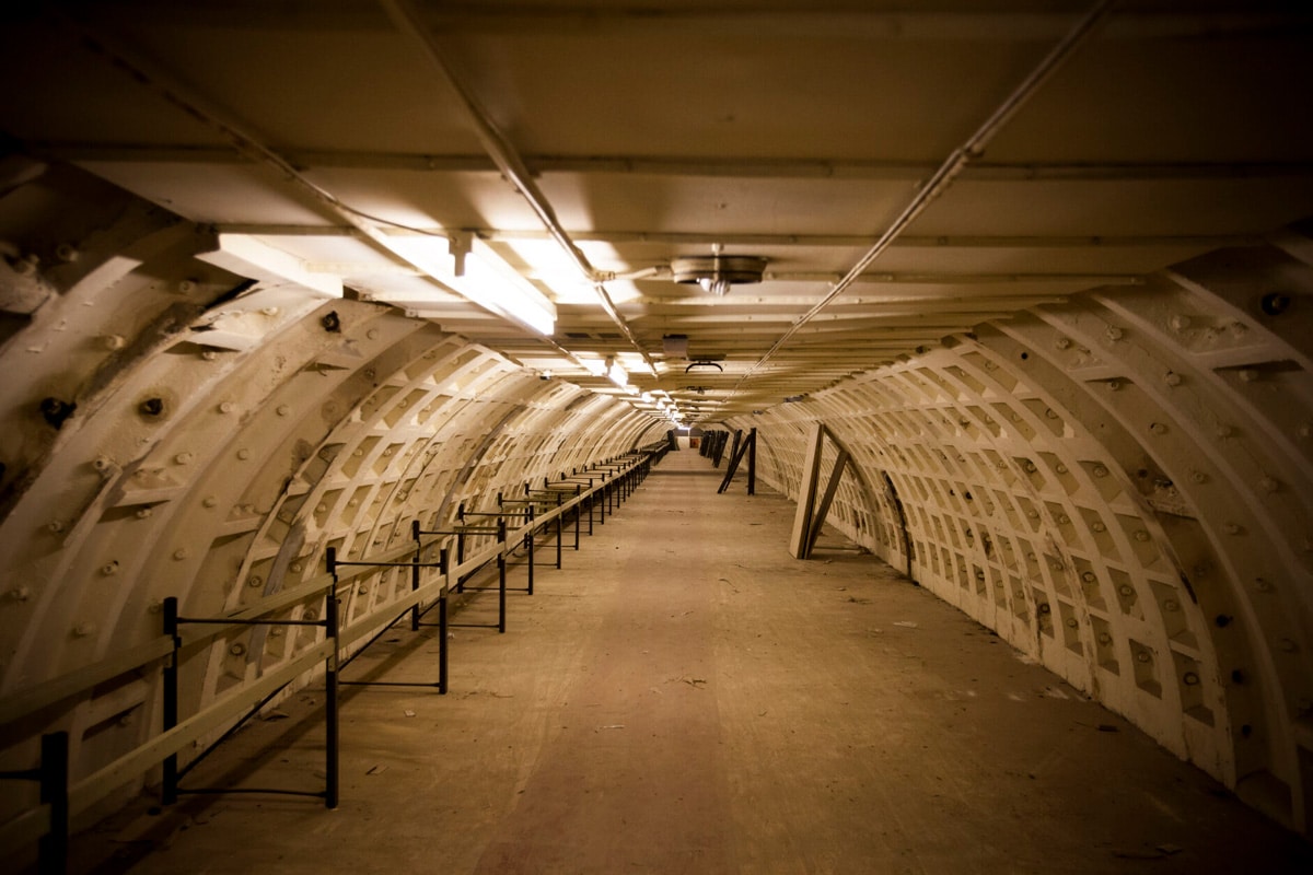 A long white-ribbed tunnel in the Clapham South deep-level shelter receding into the distance behind metal railings