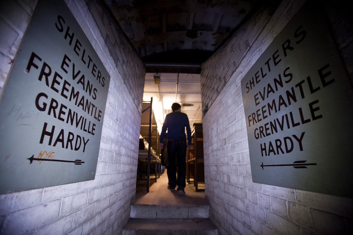 Painted signs reading SHELTERS EVANS FREEMANTLE GRENVILLE HARDY with arrows, above a stairway down into the Clapham South shelter