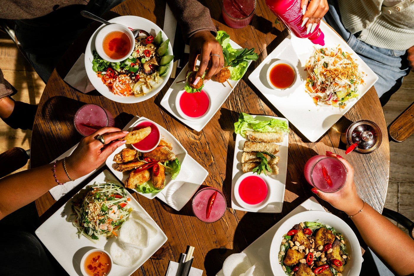 A table spread of Pho dishes with pink sriracha