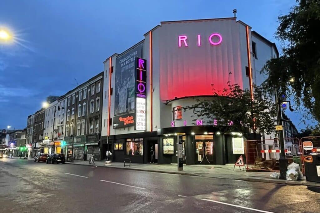 The Rio Cinema exterior lit up pink and red at dusk on Kingsland High Street
