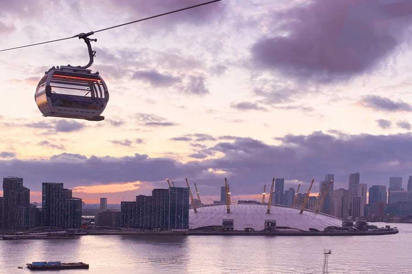 A London Cable Car cabin crossing the Thames at sunset with The O2 and the Canary Wharf skyline behind