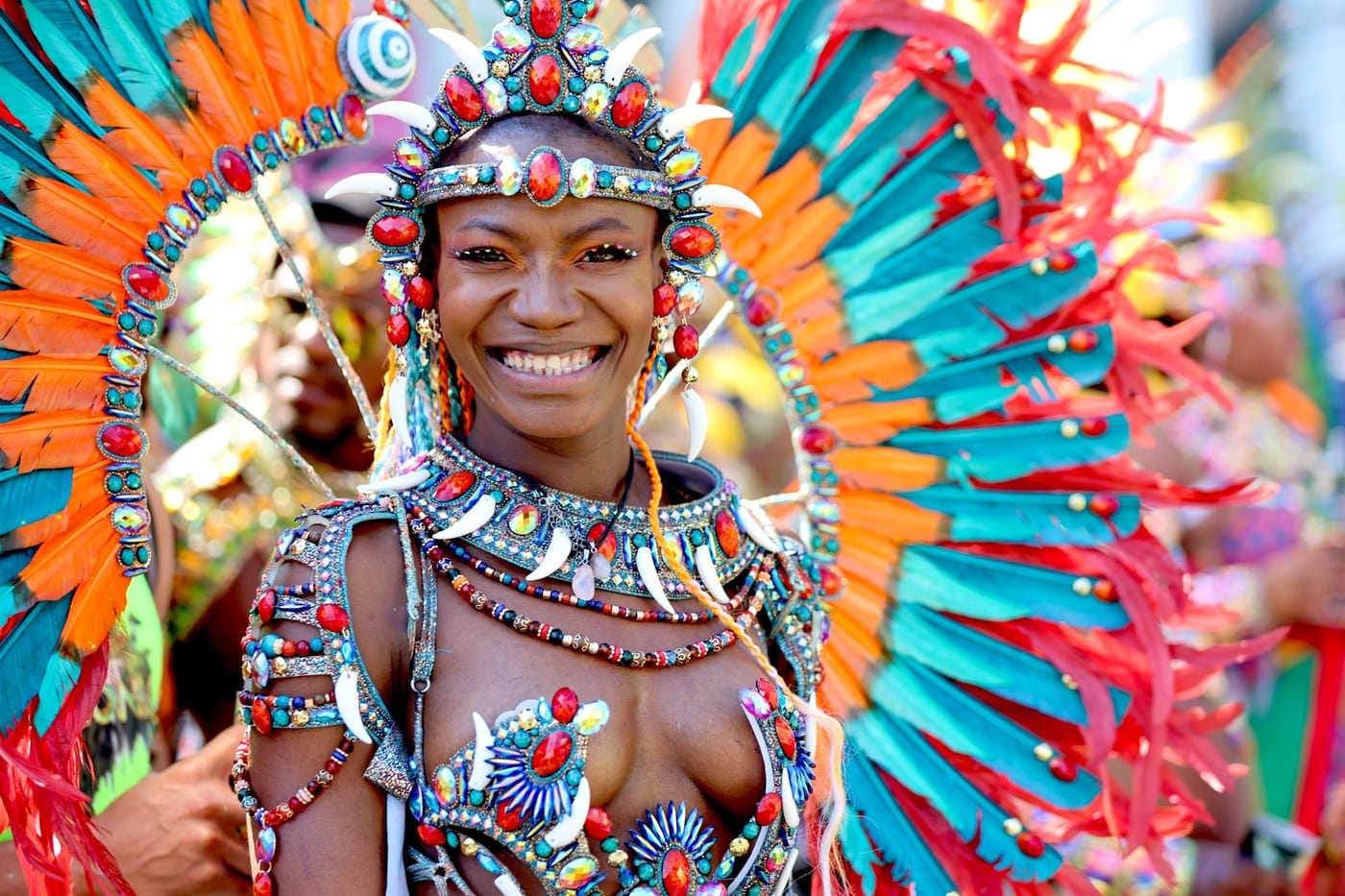 A close-up of a Carnival performer in a vivid orange, teal and red feathered headdress and beaded costume, photographed at Notting Hill Carnival 2025