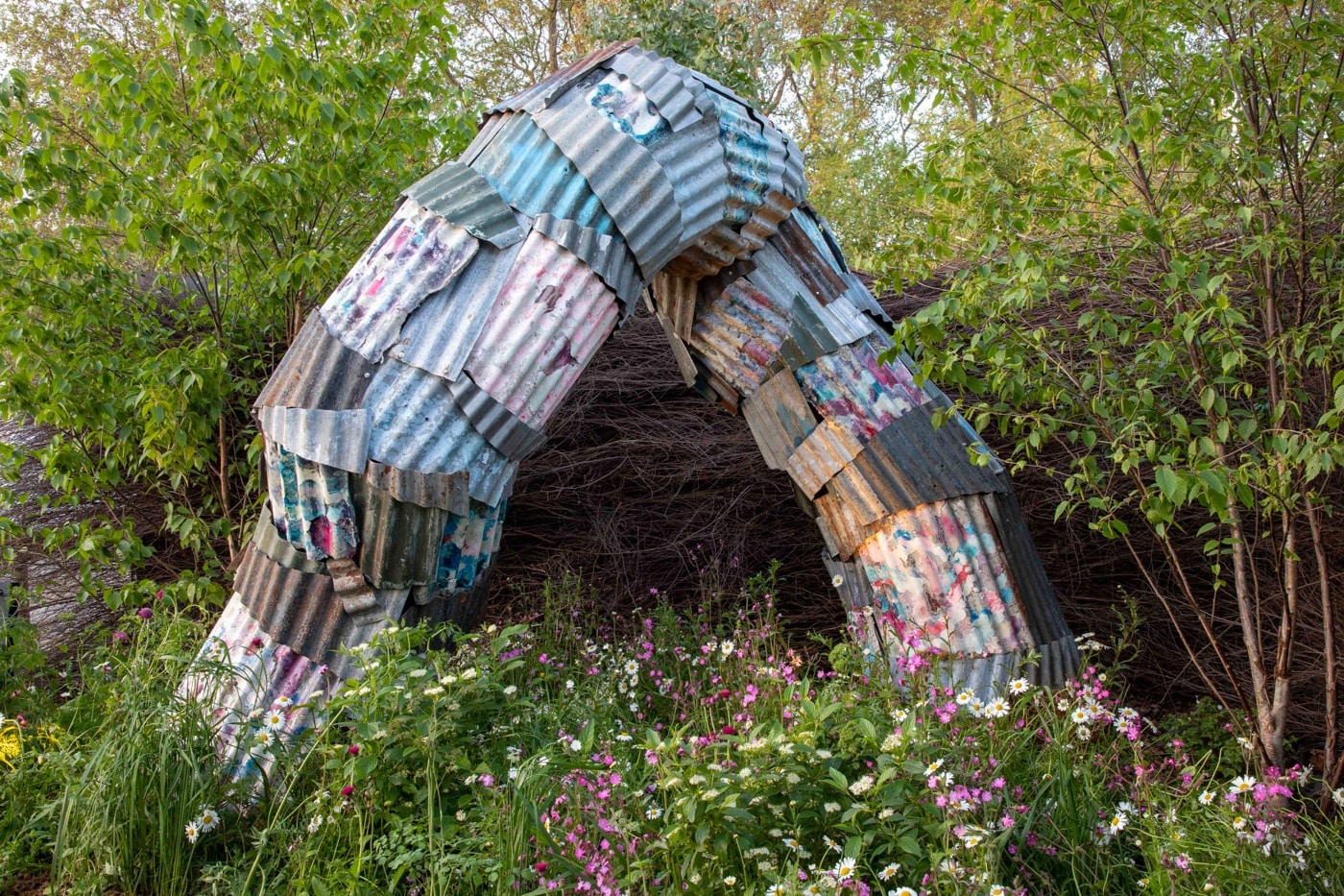 Catriona Robertson's corrugated metal arch sculpture WYRM set among wildflowers
