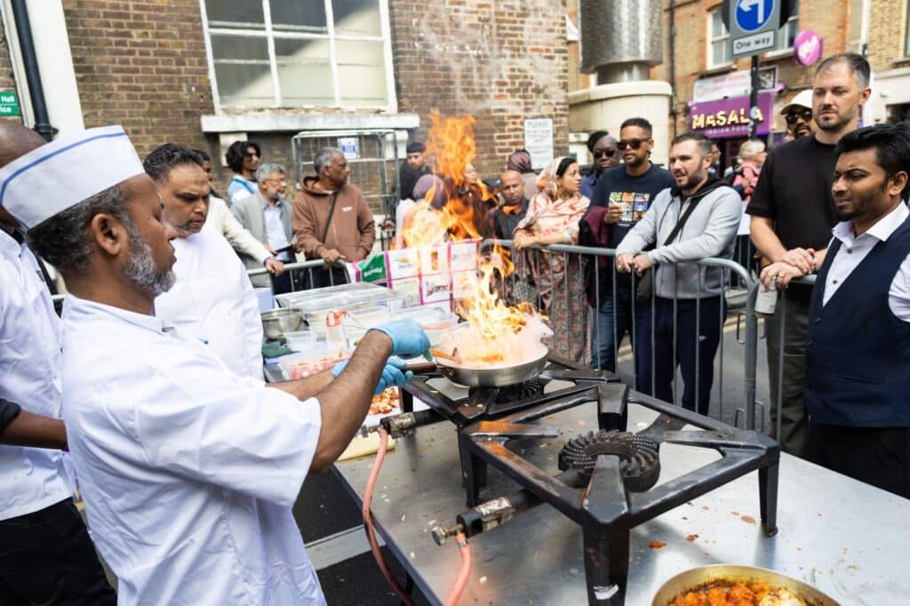 A chef cooking over an open flame at a demonstration during the Brick Lane Curry Festival