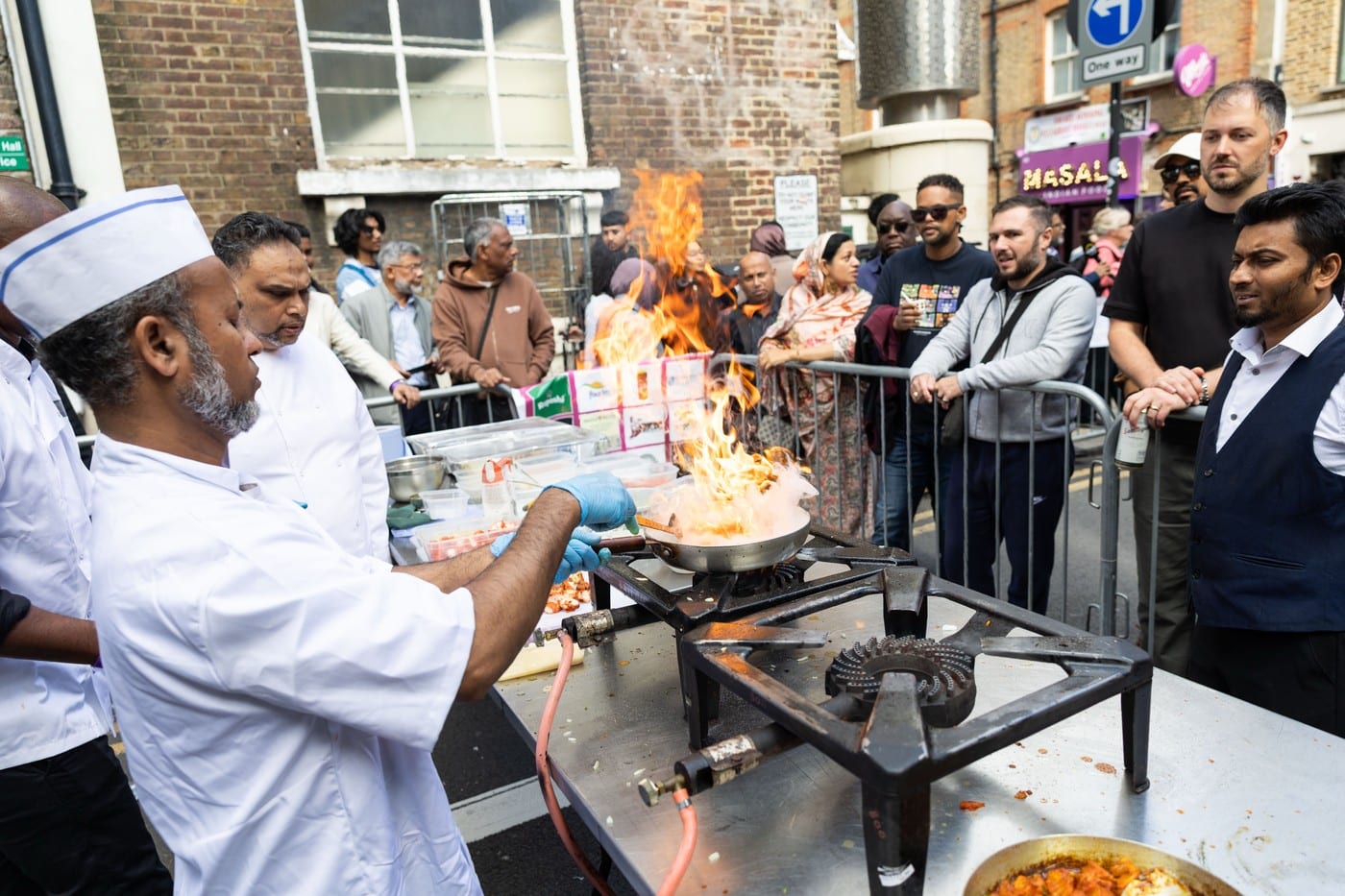 A chef flambes a dish over an open flame at a street-side cooking demonstration during the Brick Lane Curry Festival