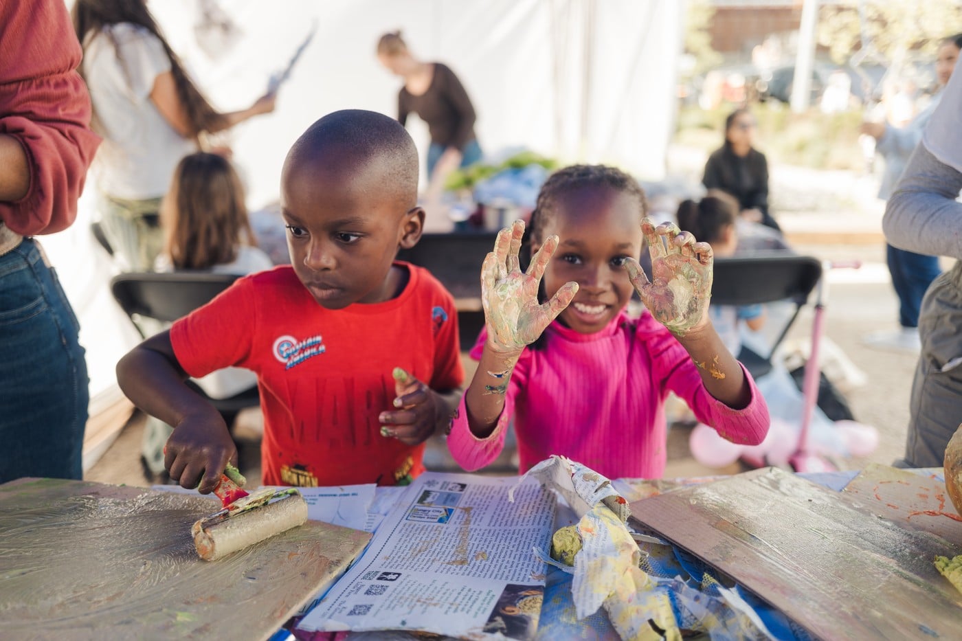 Two children show off their paint-covered hands at a printmaking workshop tent during Emerge East