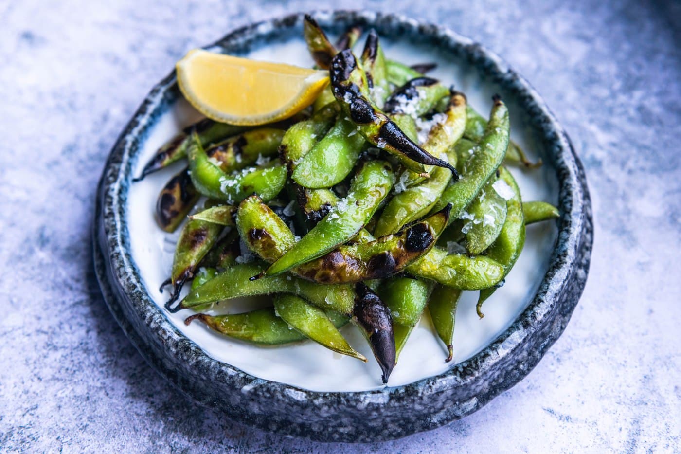 A bowl of charred, salt-flecked edamame beans with a lemon wedge at Freak Scene.