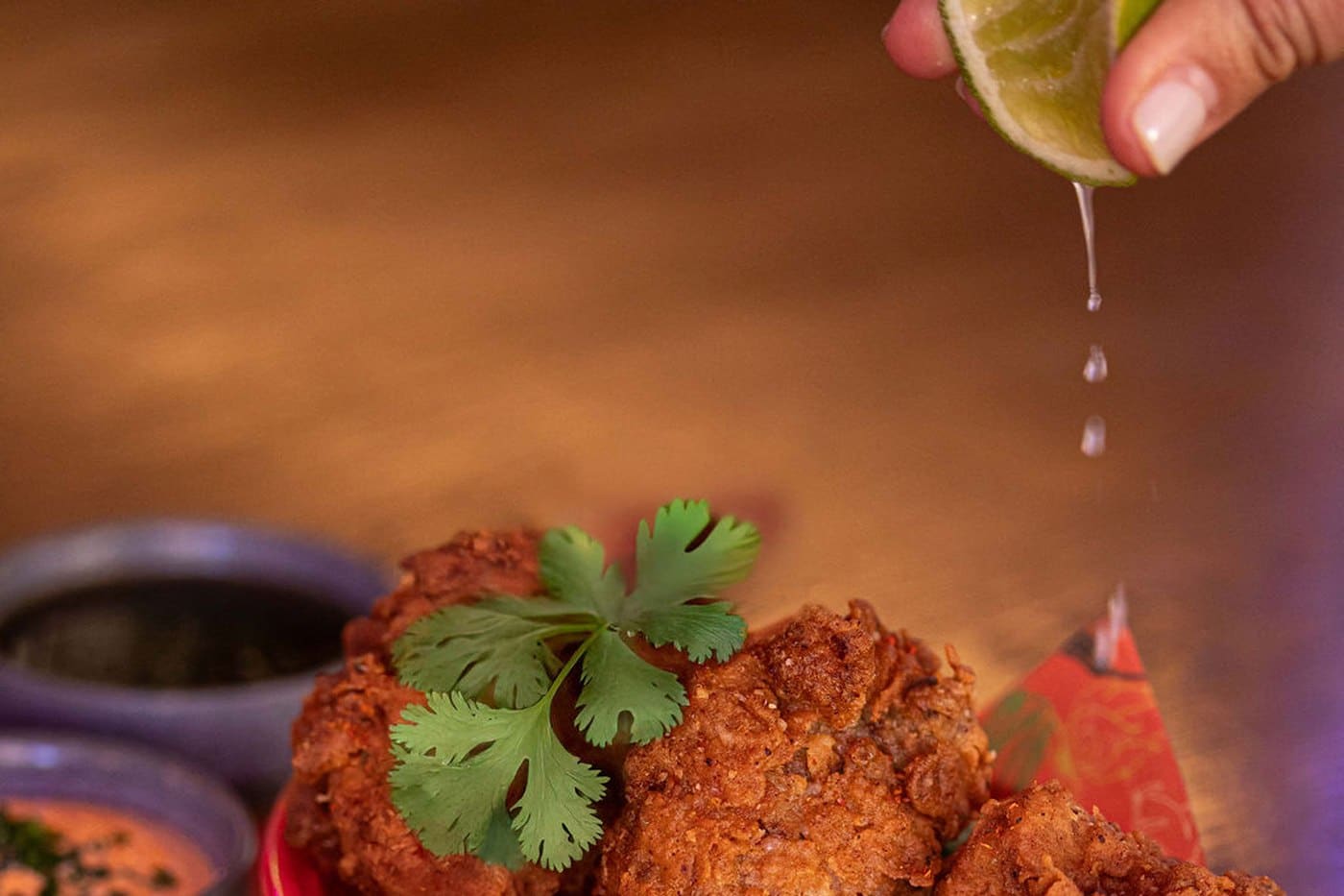 A basket of golden fried chicken karaage at Freak Scene, garnished with coriander and served with pickled cucumber and dipping sauces, with a lime squeezed over the top.
