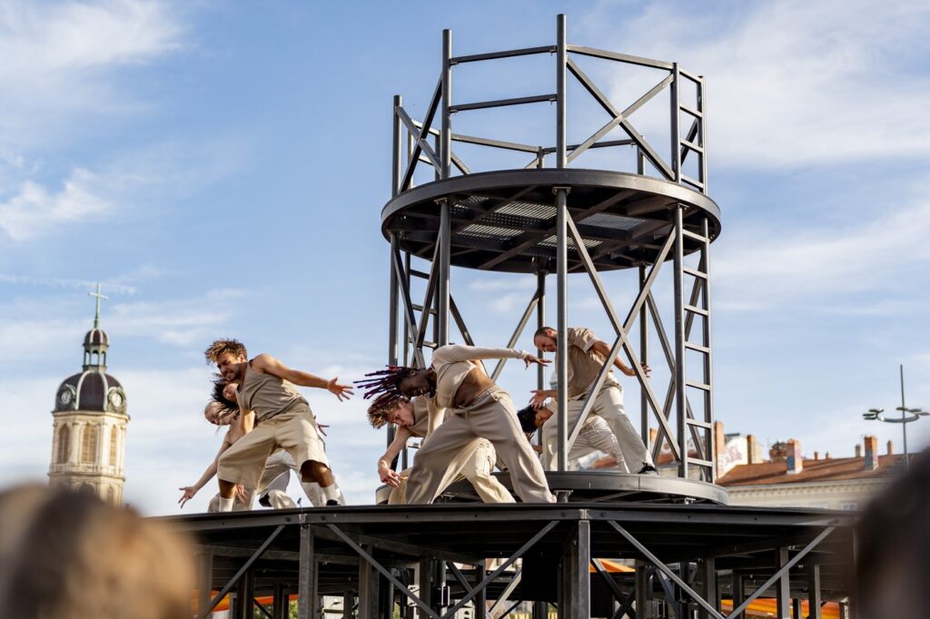 Dancers perform on a large circular steel platform above a crowd in Woolwich town centre, part of Mehdi Kerkouche's 360