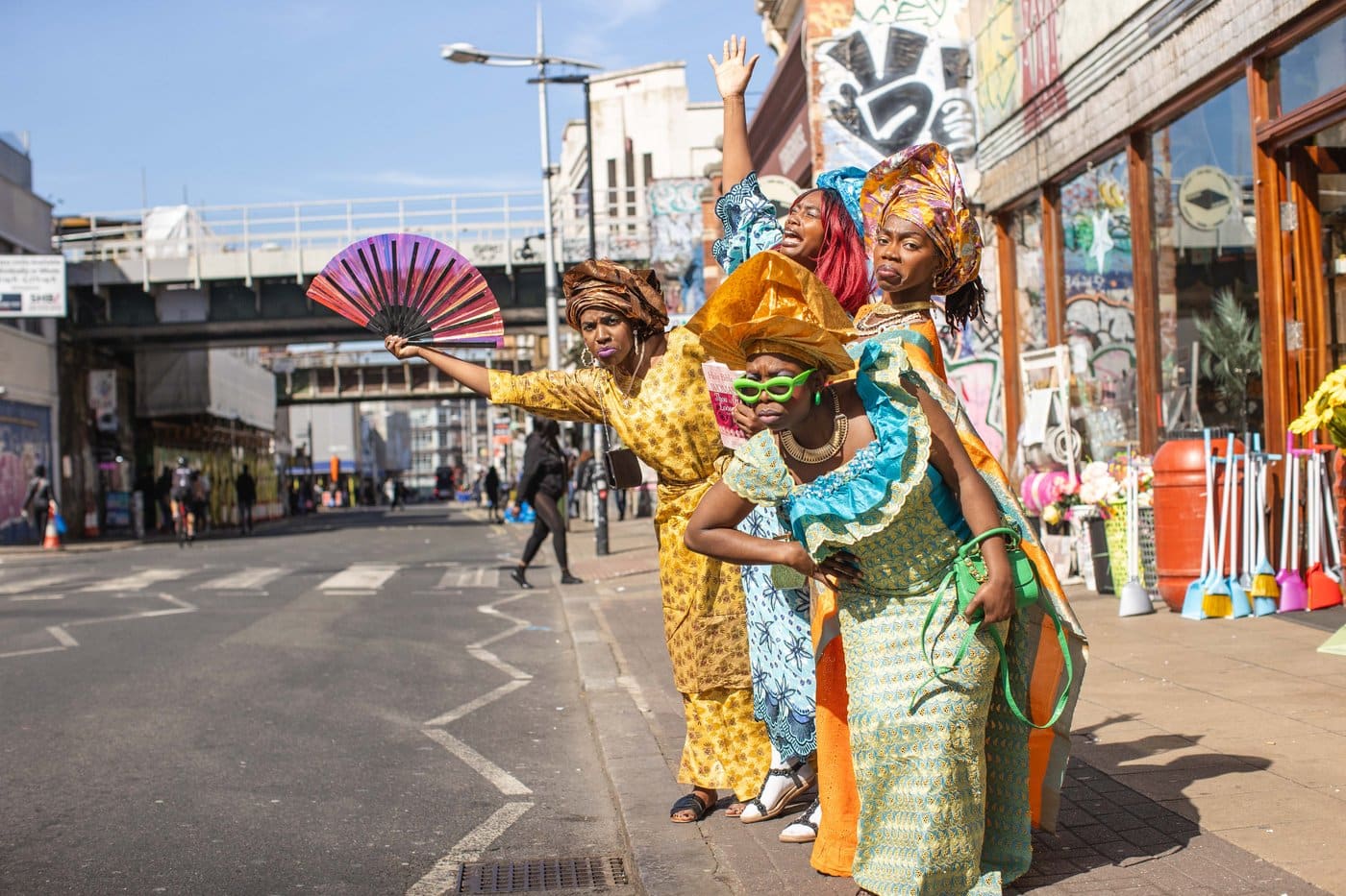Four performers in vivid West African dress and headwraps pose dramatically on a London street, part of The Aunties: The House of Masks