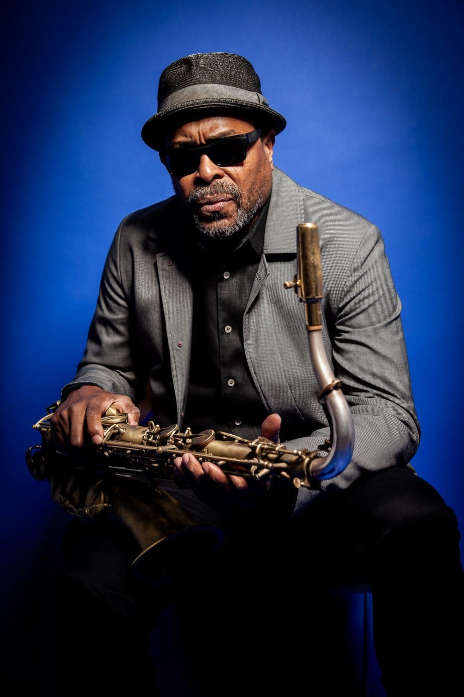 Jean Toussaint, saxophonist, wearing sunglasses and a hat against a blue background