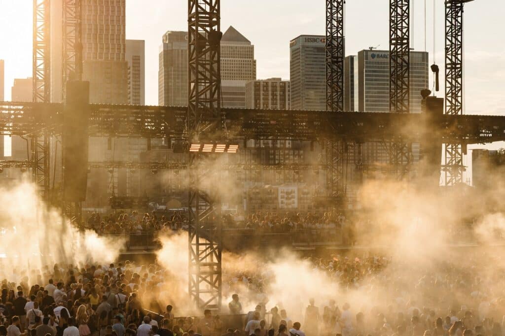 Golden-hour crowd at Magazine Open-Air on the Greenwich Peninsula, with the Canary Wharf skyline behind