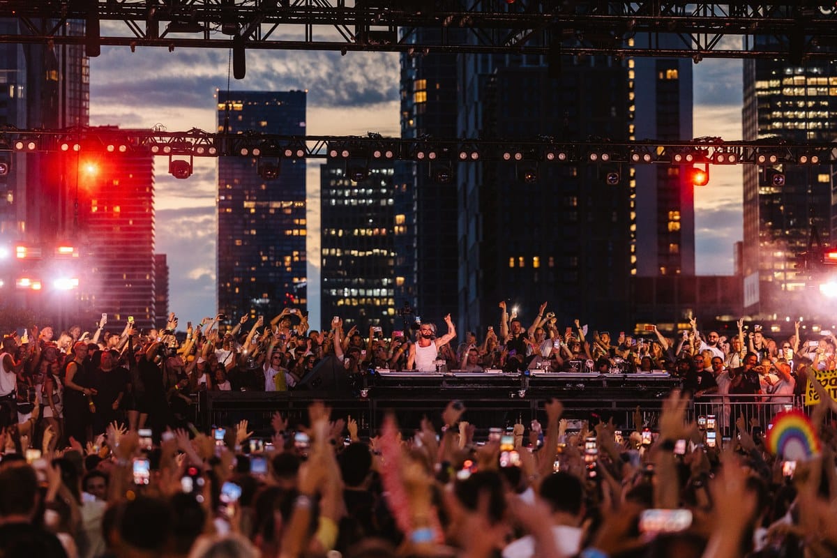 A DJ performs at dusk at Magazine Open-Air, with the crowd and Canary Wharf skyline behind
