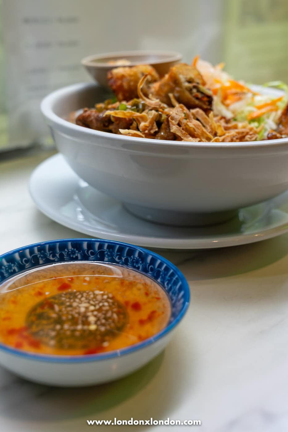 A small bowl of nuoc cham dipping sauce alongside a bowl of bun cha gio at Pho Pham