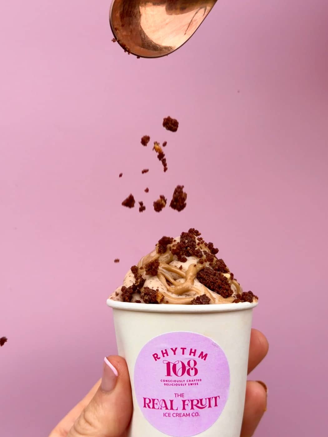 A cup of Rhythm 108 x The Real Fruit Ice Cream Co. Banana PB Cookie ice cream, topped with salted caramel spread and cookie crumble