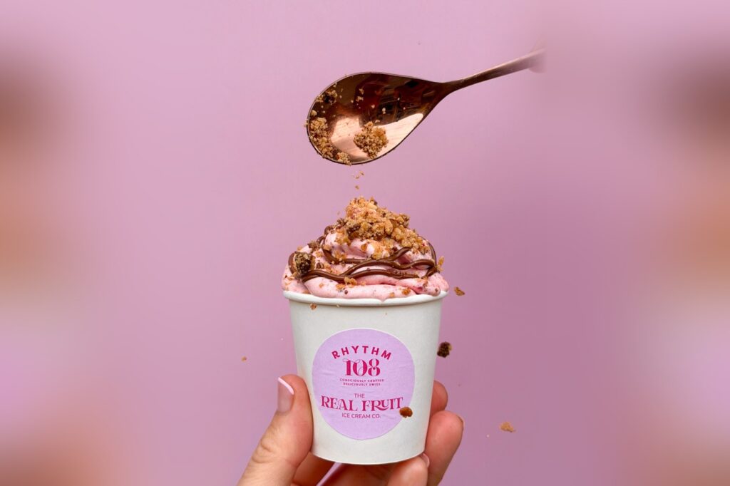 A cup of Rhythm 108 x The Real Fruit Ice Cream Co. Strawberry Choc Cookie ice cream, topped with chocolate hazelnut spread and cookie crumble