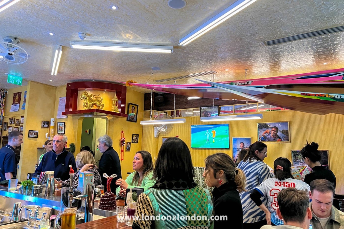 The bustling interior of Speedboat Bar, with a Thai racing boat suspended from the ceiling and diners at the bar