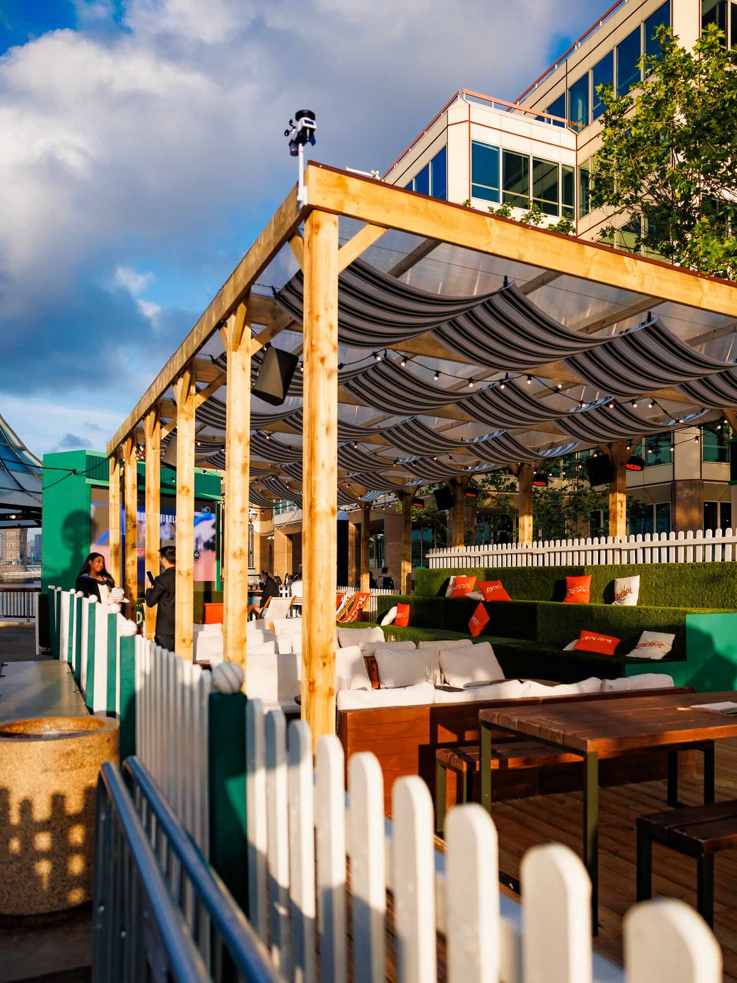 The Clubhouse's covered riverside deck at Summer by the River, London Bridge City, set up with sofas and picnic-style seating for outdoor cinema screenings
