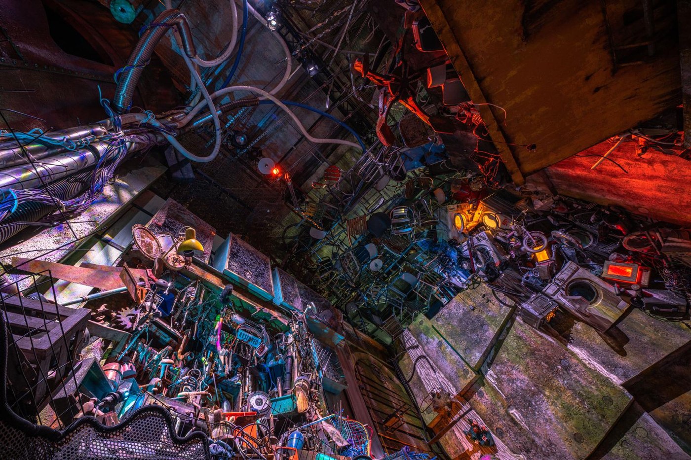 A ceiling built from salvaged chairs, bicycles, washing machines and cable, lit in red and purple