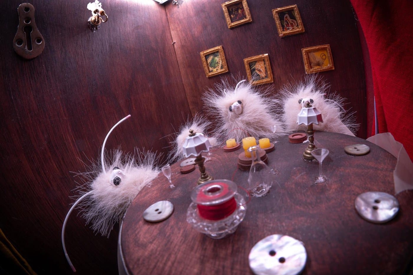 Three small fluffy creatures with wire antennae sitting around a tiny table set with button plates and thimble glasses