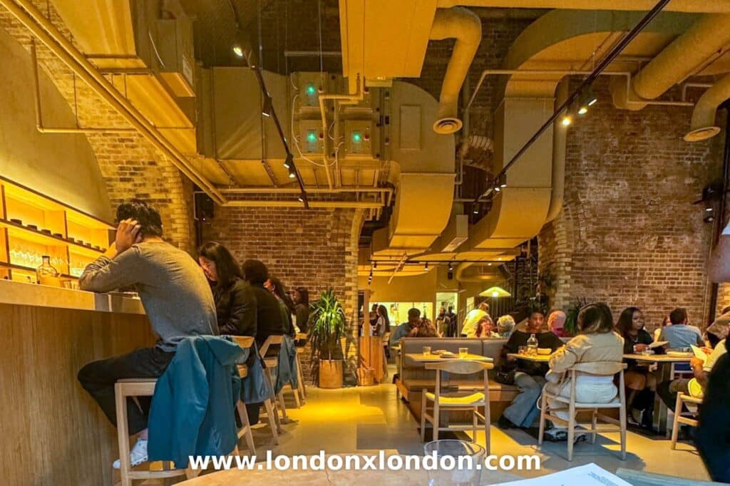 The dining room at Akara in Borough Yards, a brick railway arch with exposed ducting, counter seats along one side and tables opposite
