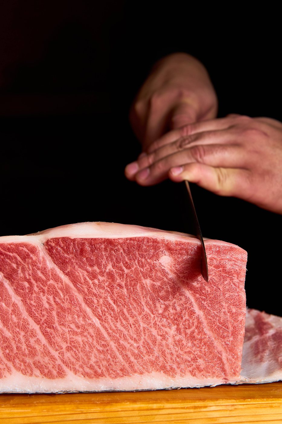 A chef slicing into a thick block of heavily marbled bluefin tuna belly on a wooden board