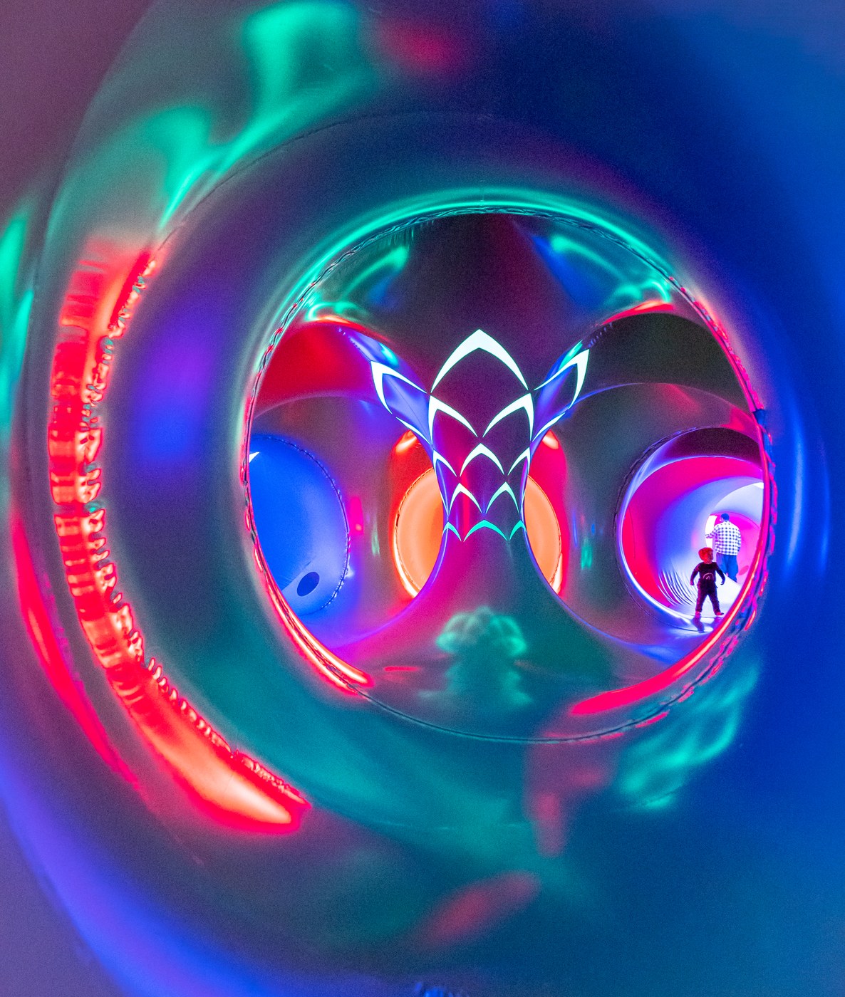 Concentric glowing tunnels in blue and pink inside ARBORIALIS with a small child visible in the distance