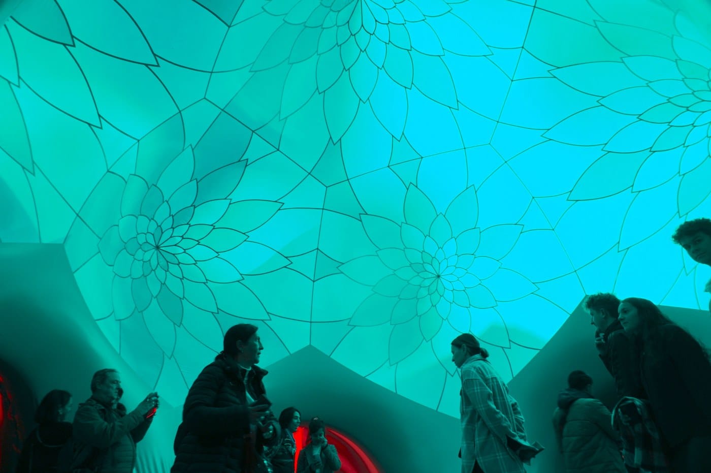 Visitors silhouetted beneath a turquoise dome patterned with overlapping flower shapes inside ARBORIALIS