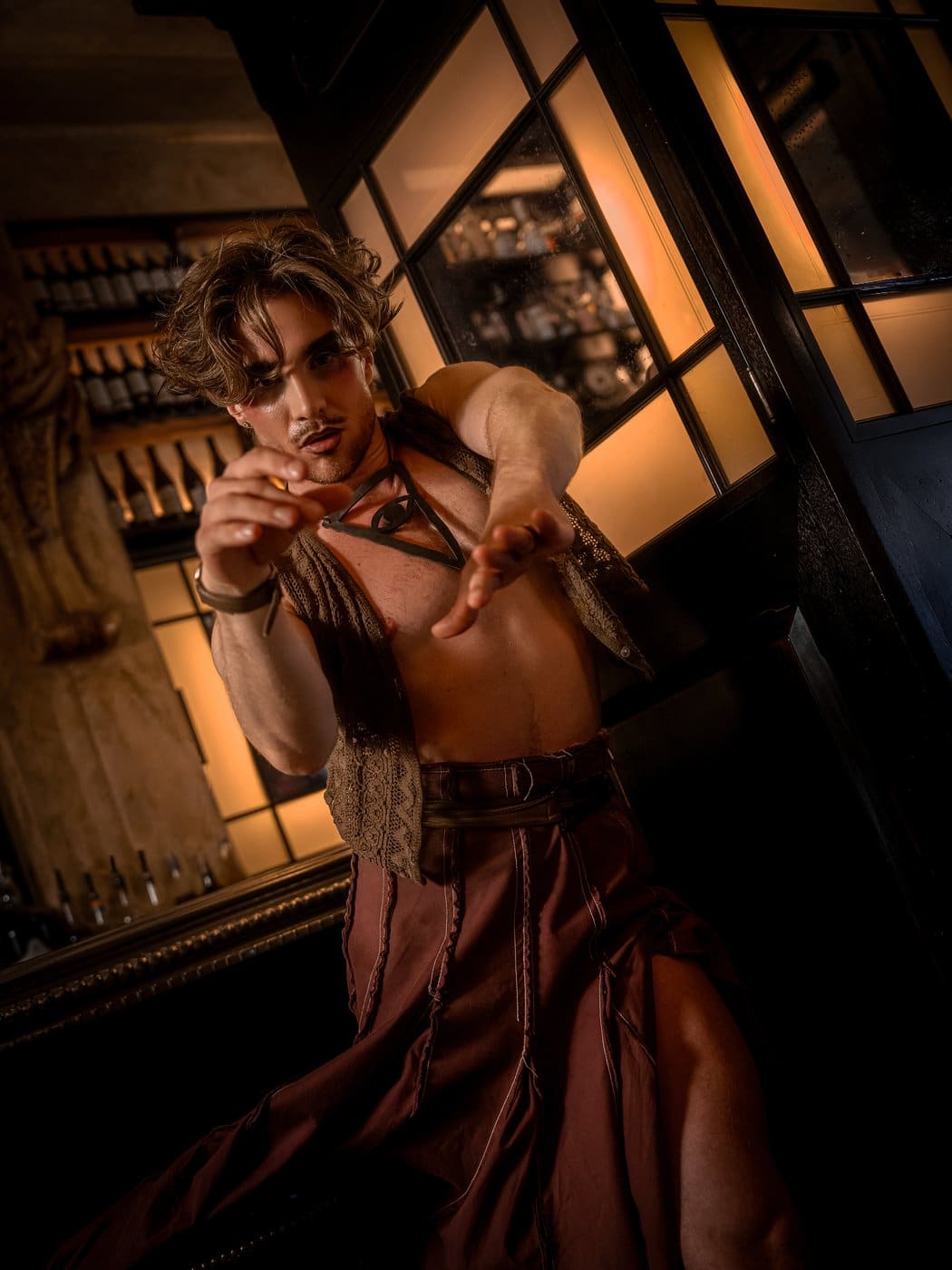 A Cabaret Prologue performer in a lace waistcoat and long skirt reaching towards the camera beside the mirrored bar at Balthazar