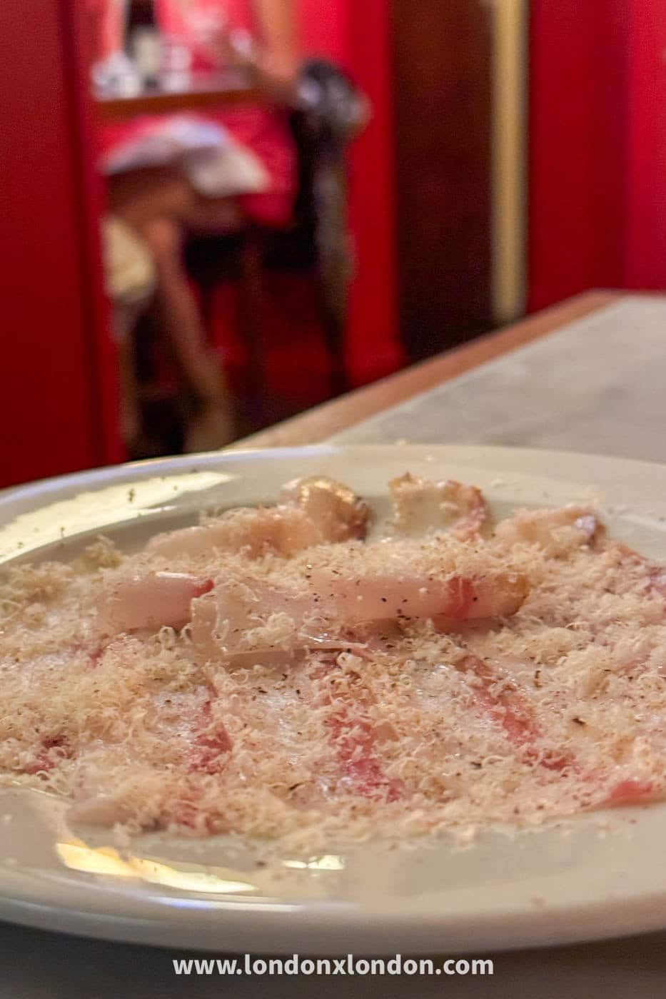 A plate of pale pink sliced seafood under a heavy blizzard of finely grated hard cheese and black pepper at Camille in Borough Market