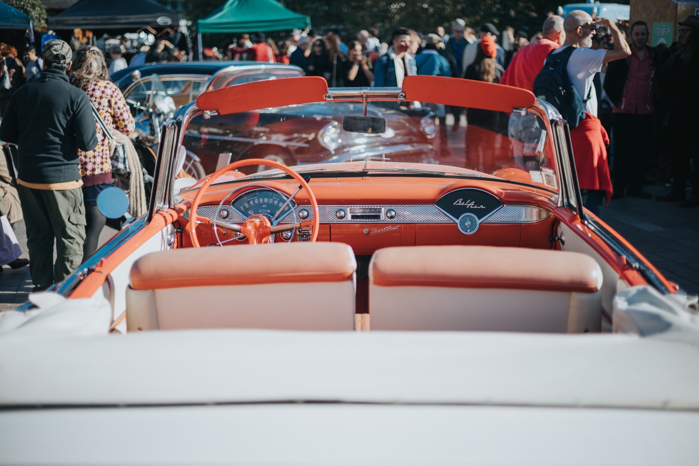 The orange dashboard and steering wheel of a Chevrolet Bel Air convertible with crowds behind