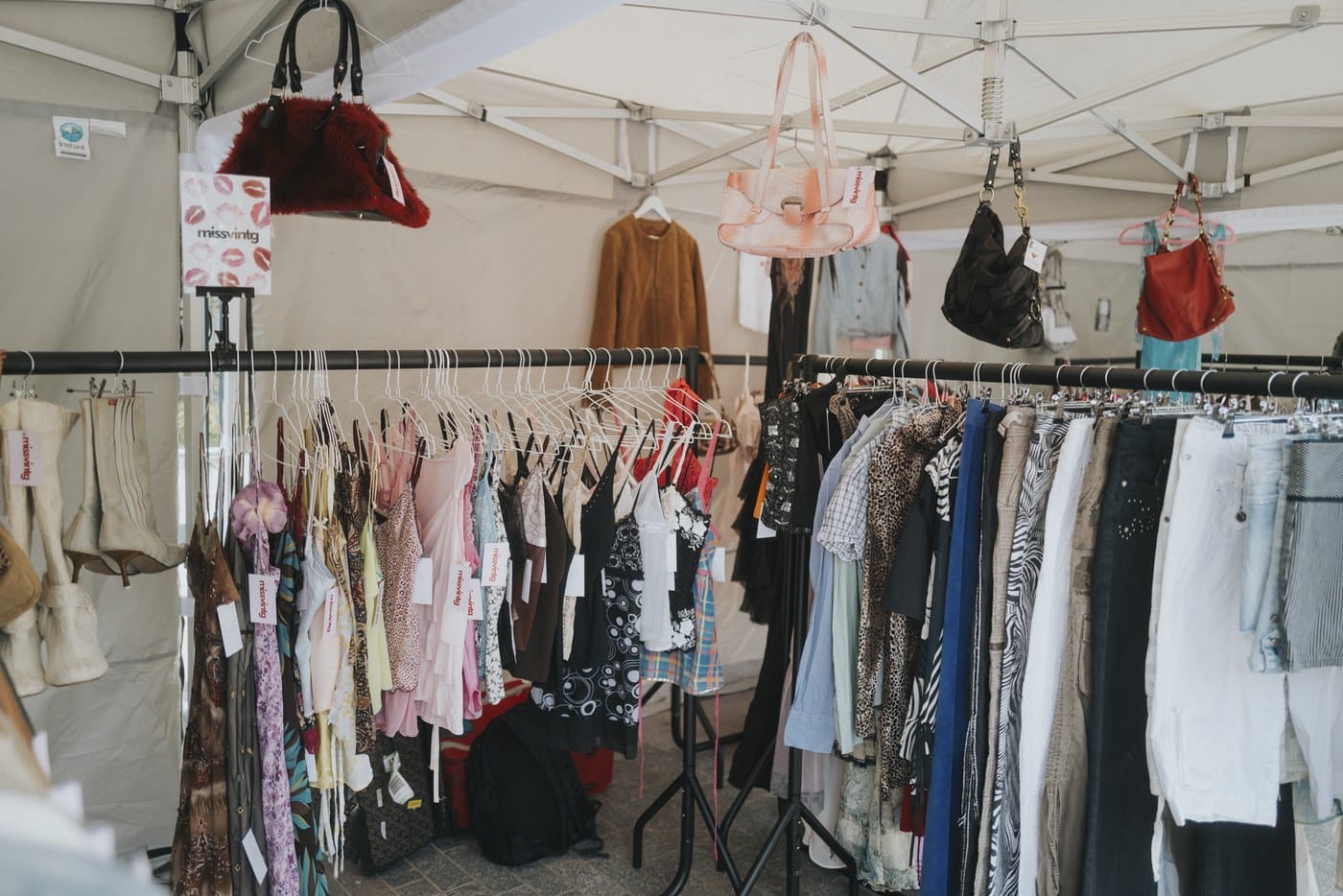 Rails of vintage clothing and hanging handbags inside a covered market stall