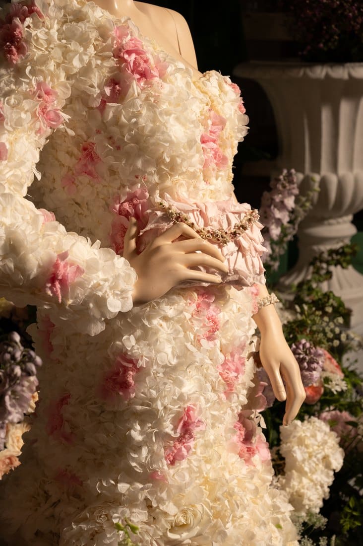 Detail of a gown built from preserved white hydrangea petals with pink carnations worked through it, and a bracelet of dried flowers on the wrist