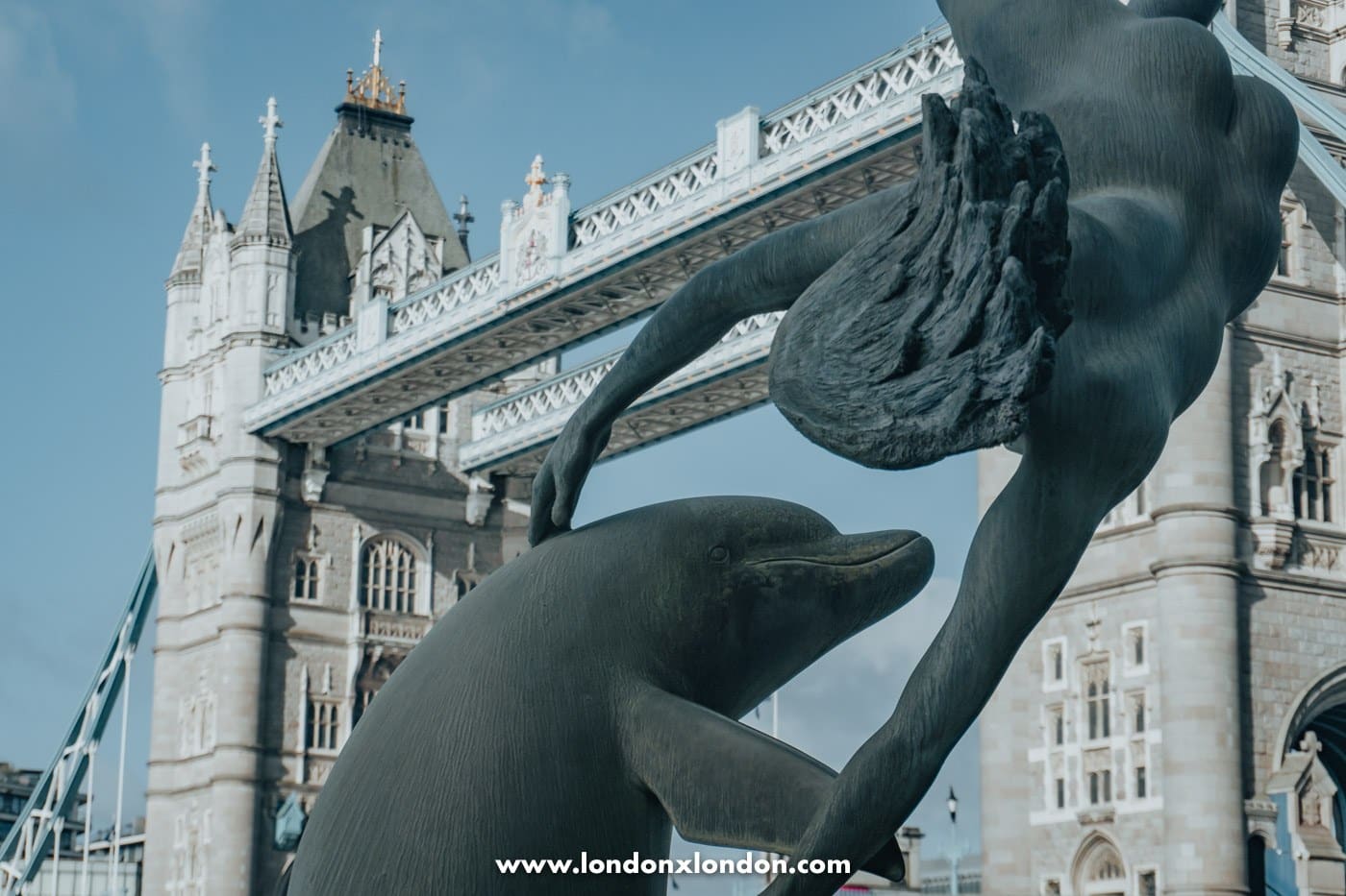 Close-up of the dolphin and the girl's outstretched arm in David Wynne's bronze sculpture by Tower Bridge