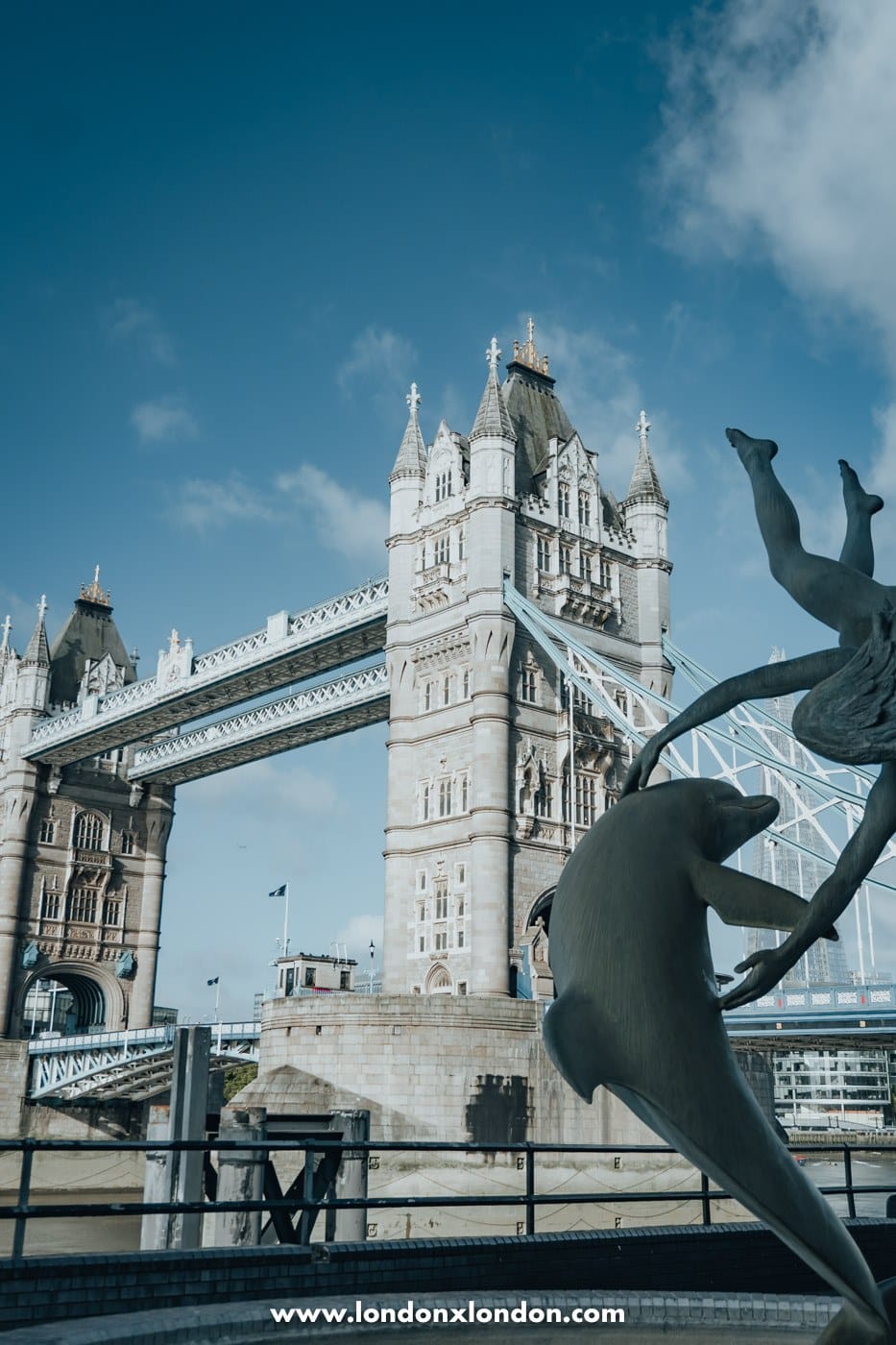 Girl with a Dolphin bronze sculpture seen from the Thames Path with Tower Bridge behind