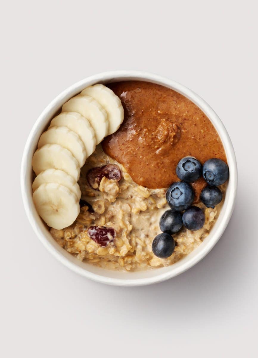 A Joe and the Juice overnight oats bowl topped with sliced banana, almond butter, blueberries and dried cranberries