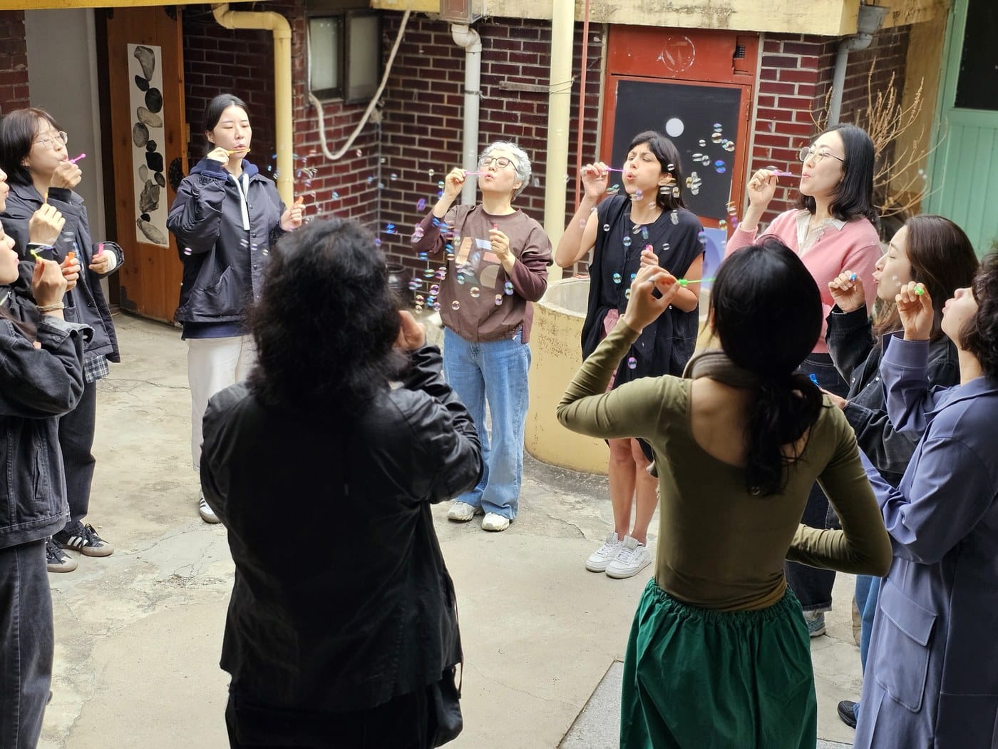 A circle of people outdoors blowing bubbles together during a workshop