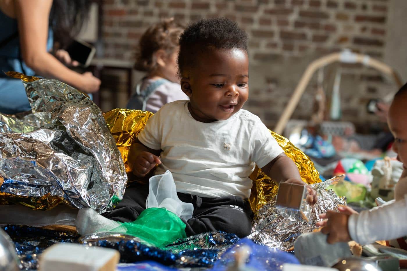 A baby sitting on gold and silver foil surrounded by sensory materials at a Little Londoners session at London Museum Docklands