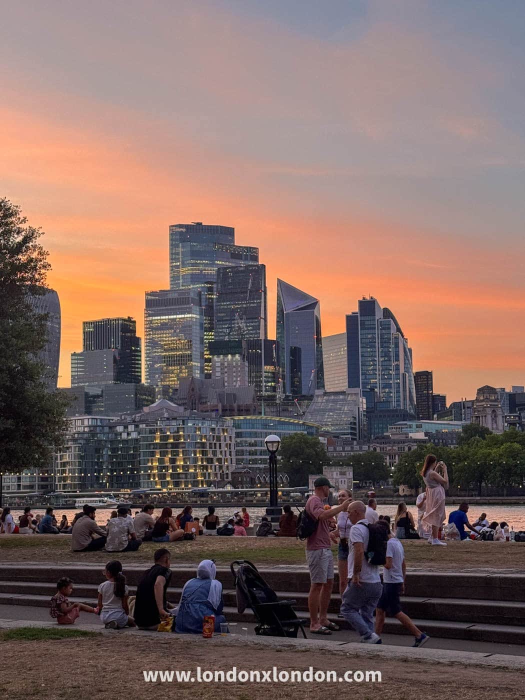 Crowds watching the sunset over the City of London skyline from the Thames path