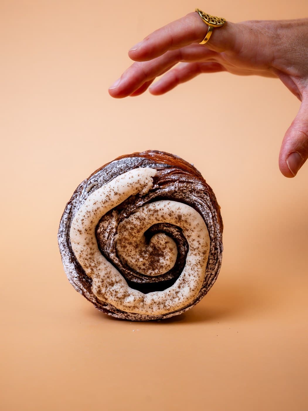 A cinnamon swirl from Okja, its cream-piped spiral dusted with cinnamon, with a hand reaching down towards it