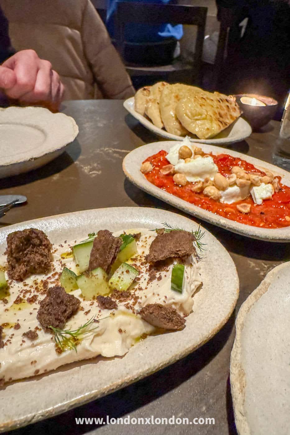 Mezze at OMA in Borough Market: a whipped dip scattered with cucumber and dill, a plate of charred flatbread and a roasted red pepper dish with soft cheese and chickpeas, on a metal table by candlelight