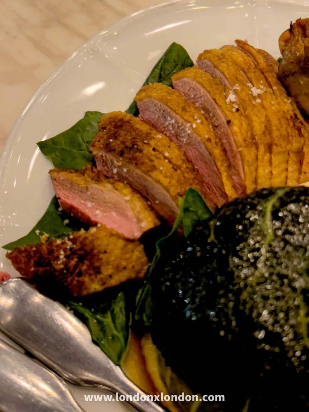 Sliced pink duck breast with crisp skin and sea salt flakes, fanned over spinach on a large white sharing plate at Pique-Nique