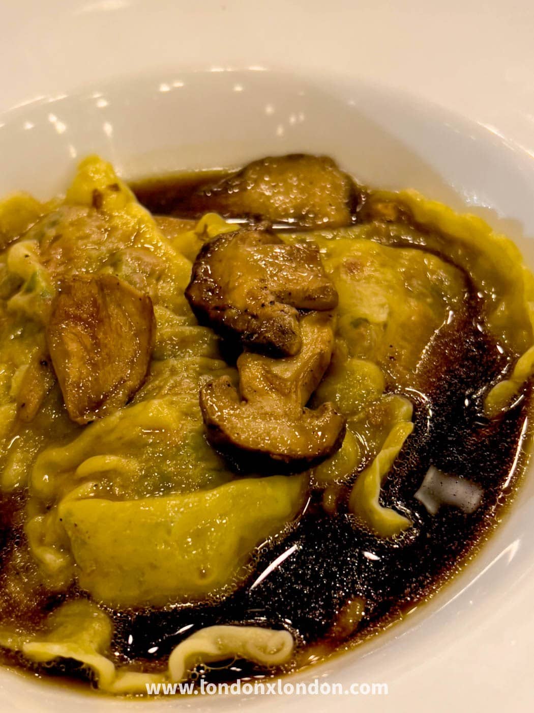 Filled pasta parcels at Pique-Nique in a dark glossy broth with sauteed mushrooms, served in a white bowl