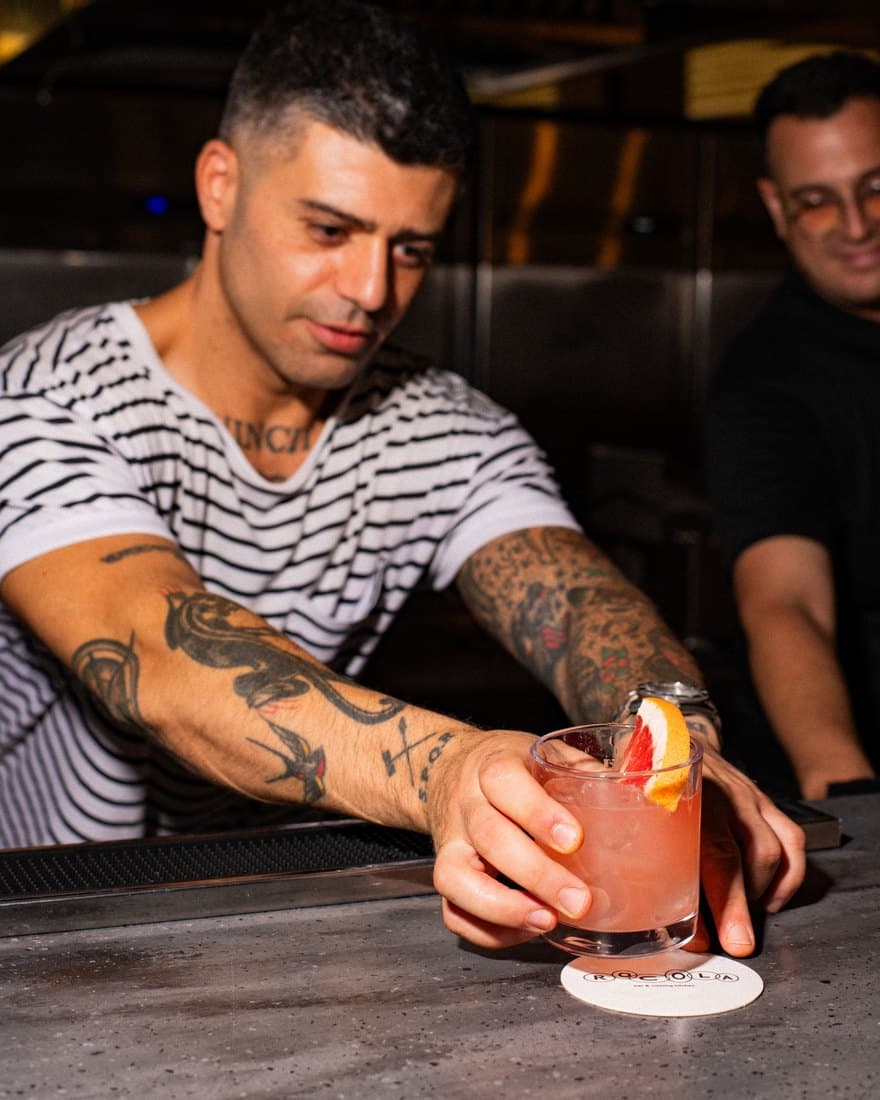 A bartender at Rocola sliding a pink grapefruit cocktail across the concrete bar onto a Rocola coaster