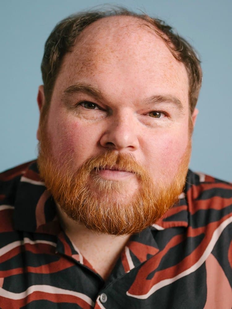 Actor Stephen Collins, who plays Roland in Constellations, photographed against a pale blue background in a patterned shirt