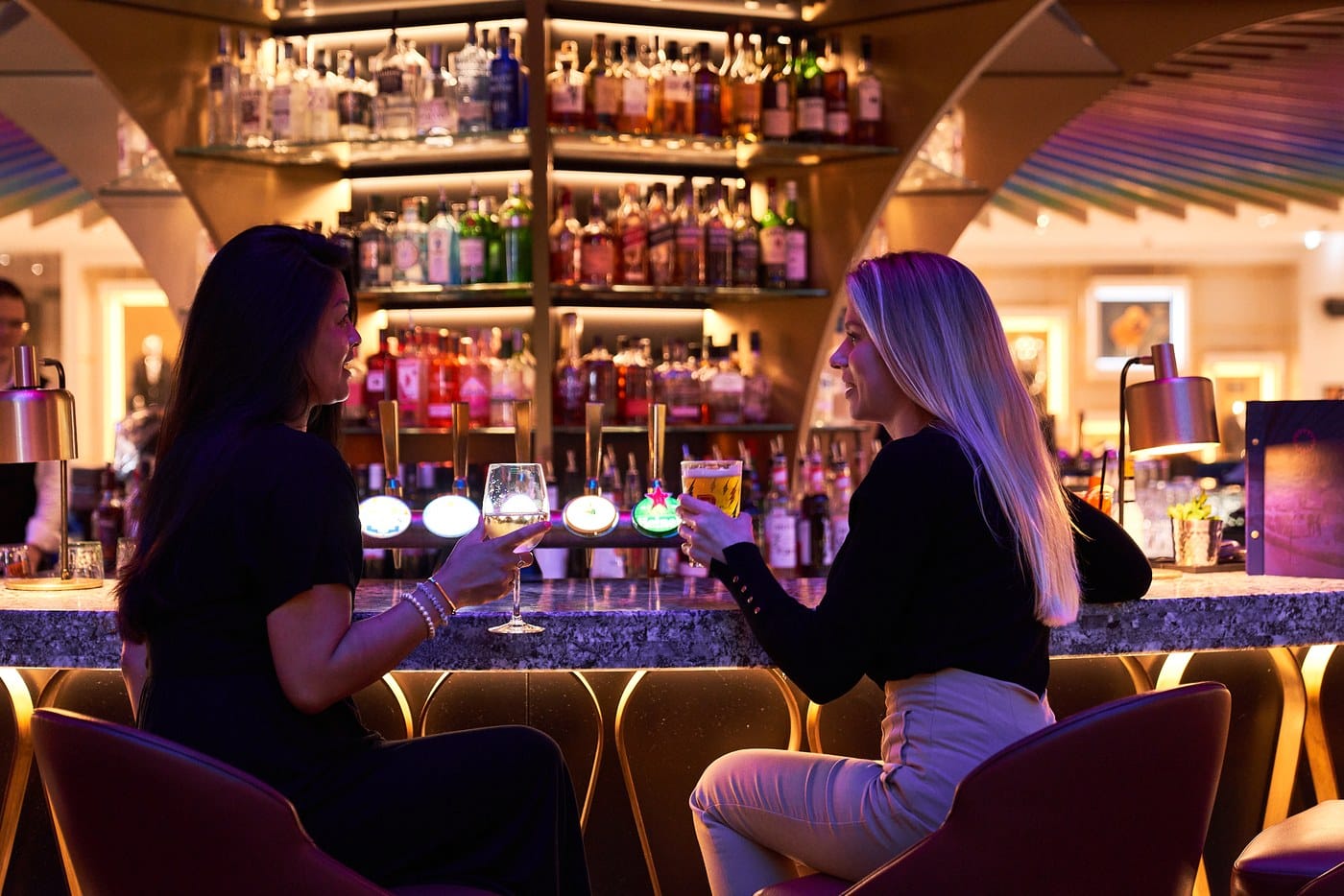 Two people with drinks at the lit bar in SOUND at The Cumberland