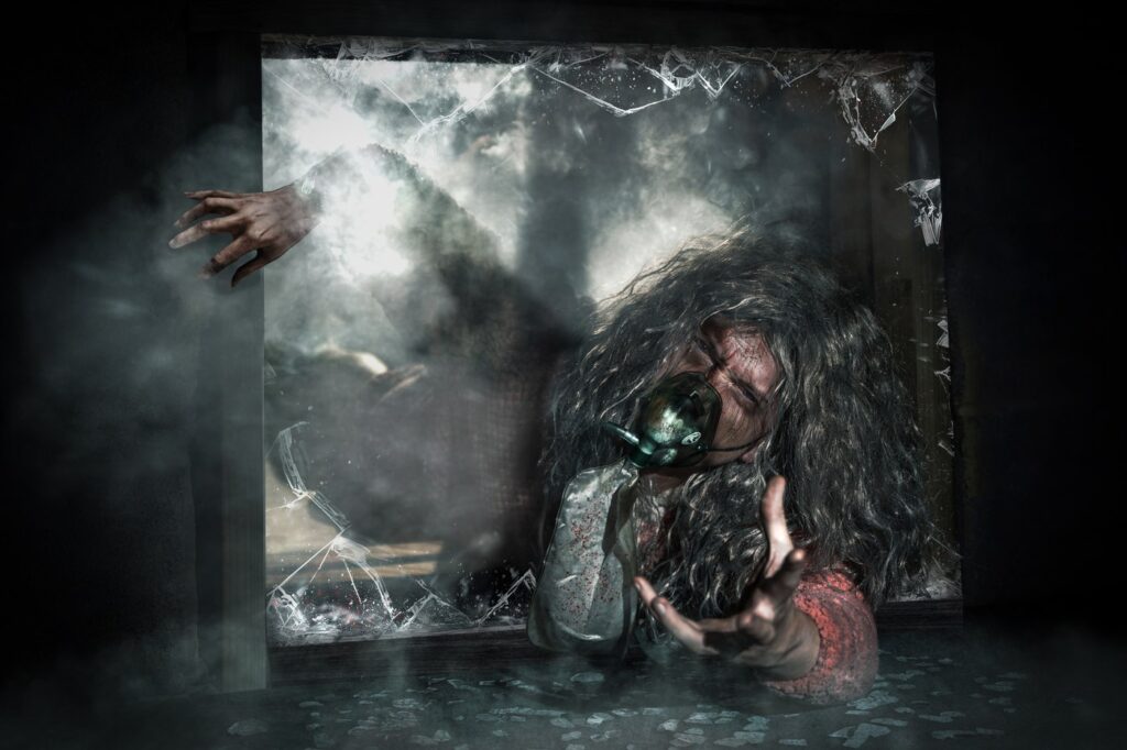 A figure in an oxygen mask with wild grey hair reaching through a smashed window in a dark smoke-filled room