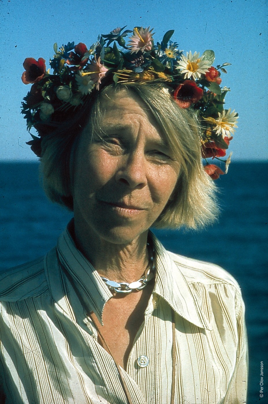Tove Jansson wearing a crown of wild flowers, photographed against the sea